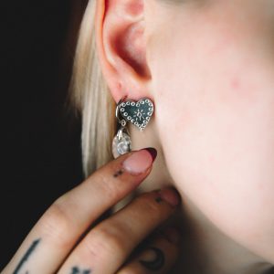 young white woman with tattoos holding her neck with a stamped heart stud earrings