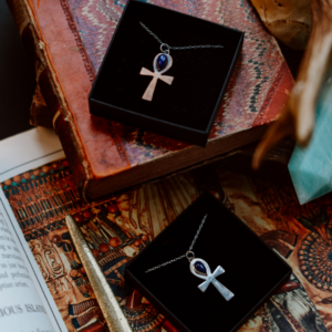 copper and silver ankh shaped pendants laid on old books with Egyptian imagery