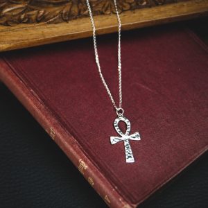 sterling silver ankh necklace with a sterling silver chain laid on top of a dark red old fashioned book with a wooden background