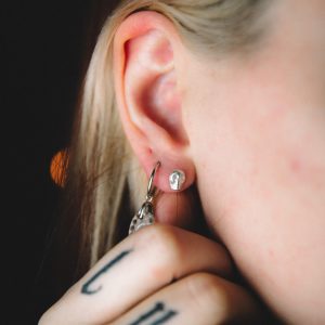 young white woman with tattoos holding her neck with a stamped tiny skull stud earring