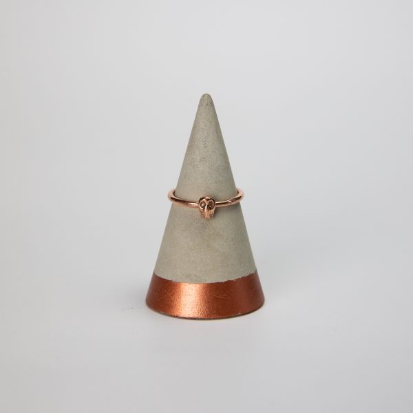 copper ring band with small copper skull sat on a concrete ring holder with a white background