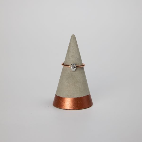 copper ring band with small silver skull sat on a concrete ring holder with a white background