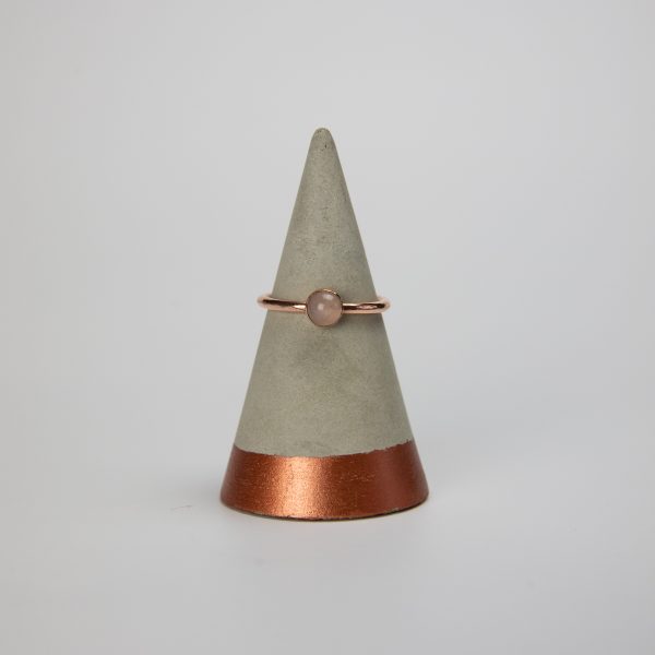 rose quartz copper gemstone ring sat on a concrete ring holder with a white background