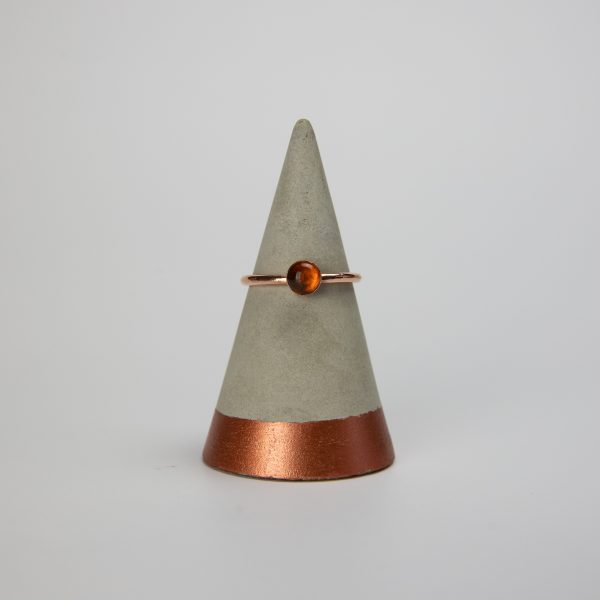 amber copper gemstone ring sat on a concrete ring holder with a white background