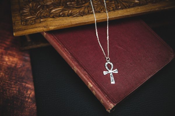 sterling silver ankh necklace with a sterling silver chain laid on top of a dark red old fashioned book with a wooden background