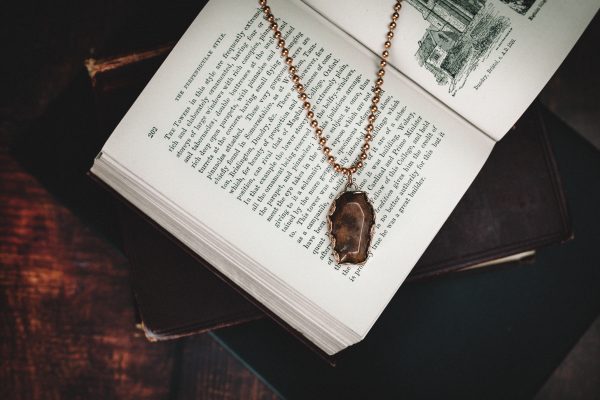sunstone coffin necklace made from copper with a copper ball chain necklace laid on a open old fashioned book with other books beneath