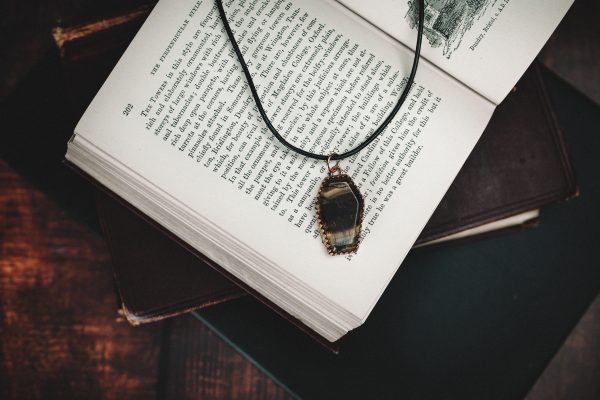tigers eye coffin necklace made from copper with a black thong necklace laid on a open old fashioned book with other books beneath