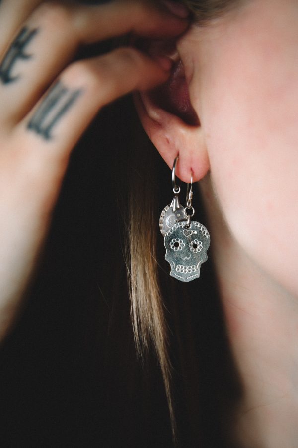young white woman with tattoos holding her hair with a stamped sugar skull dangly skull earring in silver