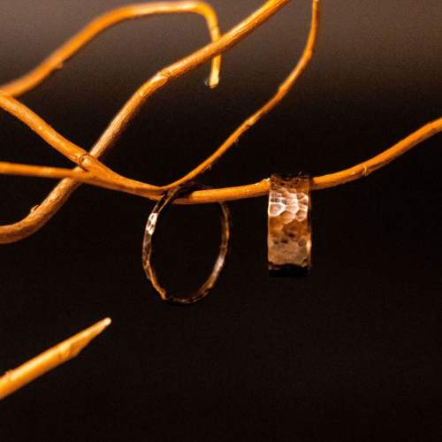 Two copper rings sat on a red ribbon on a table with fairy lights behind