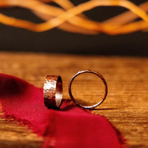 Two copper rings sat on a red ribbon on a table with fairy lights behind