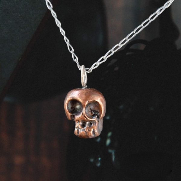 copper skull necklace on a silver chain on a dark background
