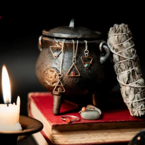 Fire, water, earth and air elemental alchemy jewellery pendants handing from a small iron cauldron with smudging stick, crystals, candle and books
