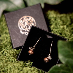 Pair of copper pumpkin earrings in black jewellery box laid on moss