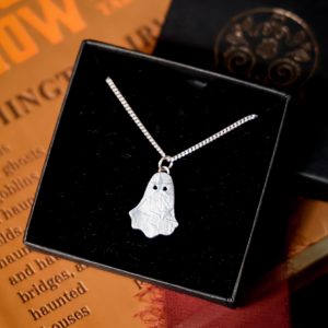 Silver ghost pendant with stars and moons pattern suspended on a sterling silver chain inside a black jewellery box lying on a yellow book