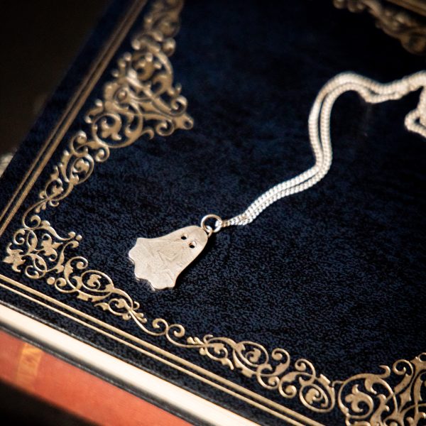 Silver ghost pendant with stars and moons pattern suspended on a sterling silver chain lying on a stack of books