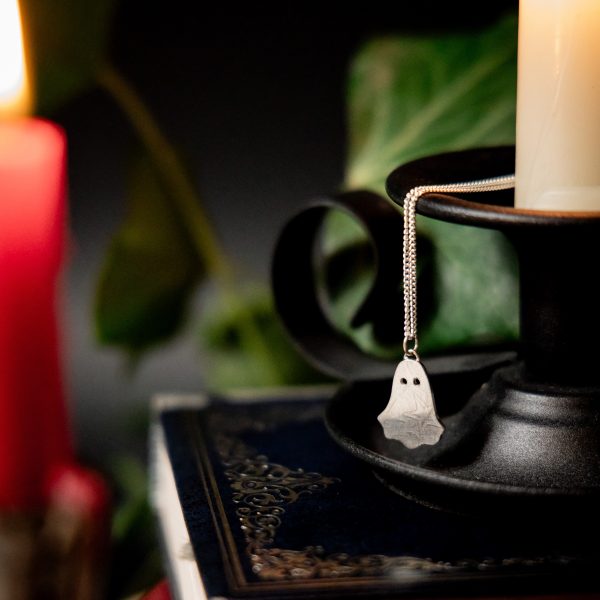 Silver ghost pendant with stars and moons pattern suspended on a sterling silver chain hanging from a white candle
