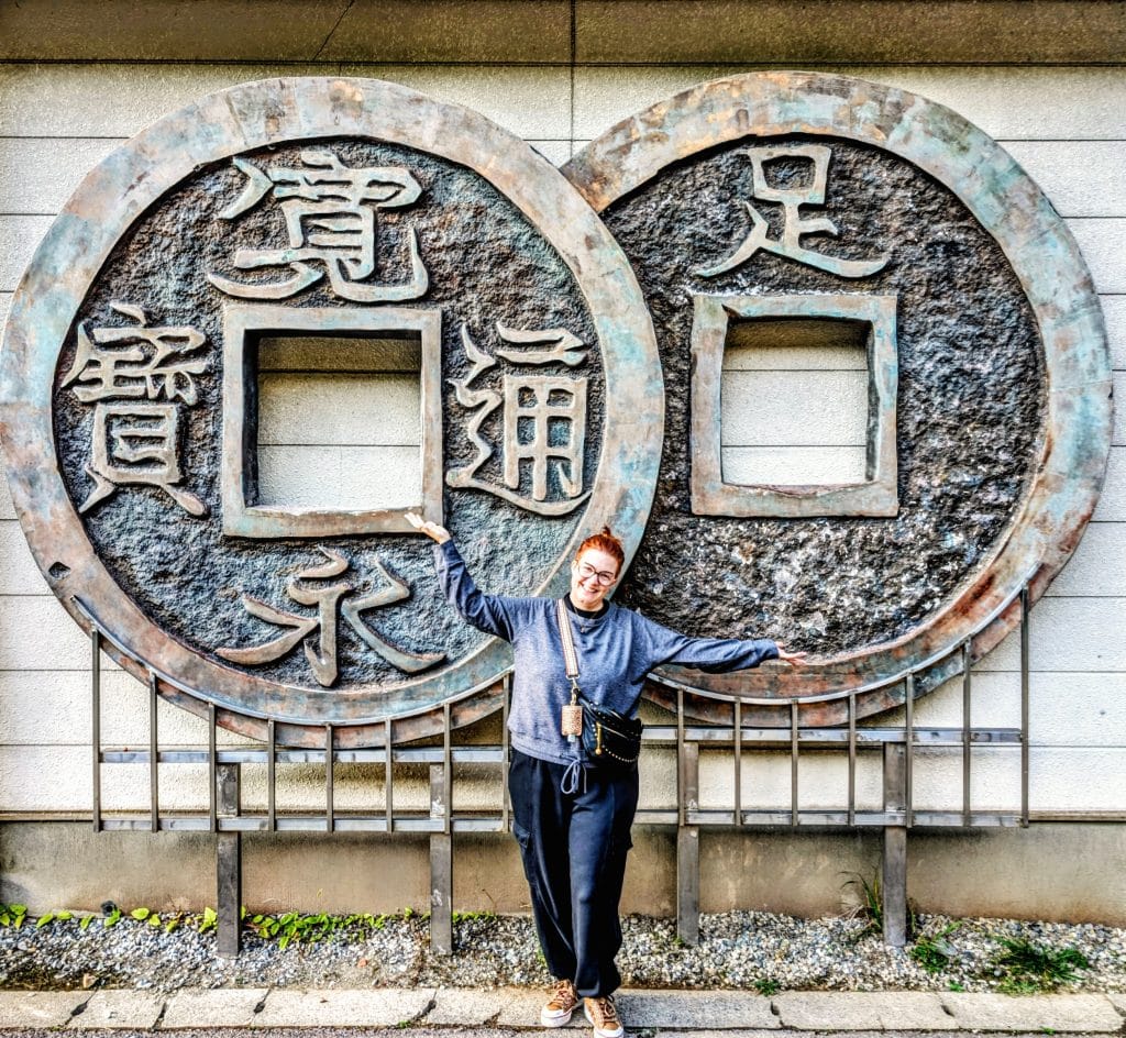 Woman stood in front of too massive copper Yen coins at Ashio Copper Mine