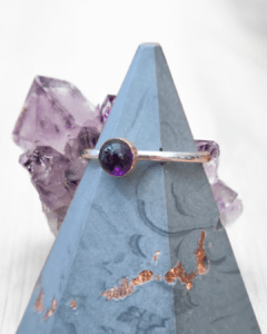 amethyst cabochon stone ring set in rose gold bezel with sterling silver band on a concrete style ring cone in front of an amethyst crystal
