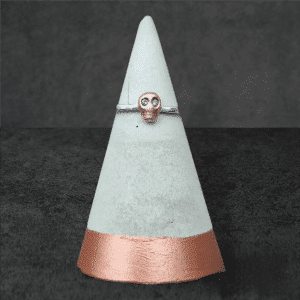 tiny copper skull ring with grey diamond eyes on silver band sat on grey concrete ring cone