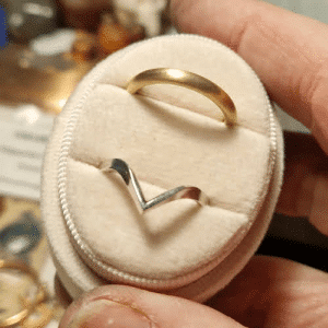 brushed yellow gold wedding band and silver wishbone band in pink ring box held in a hand