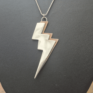 3 pronged lightning bolt necklace made from silver and copper on grey background