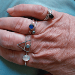 ladies hand with blue toned stone set silver and copper rings on each finger