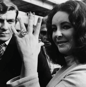 picture of lady with long dark hair holding up her left hand with a massive square cut diamond on her ring finger
