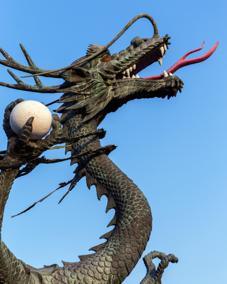 A Chinese dragon statue with it's tongue out holding a white pearl in it's claw