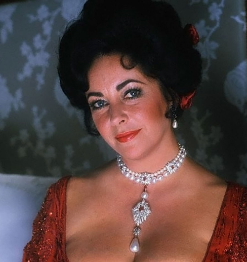 A glamours woman with dark hair in a red dress wearing a necklace made of diamonds and pearls