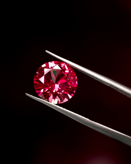 small round red crystal held in metal tweezers