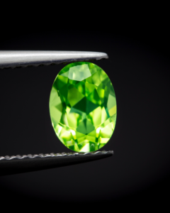 A pale green olivine coloured faceted stone held in tweezers