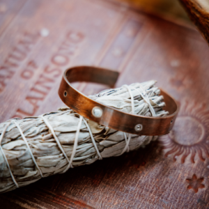 copper cuff with silver rivets sitting on a sage stick on old books