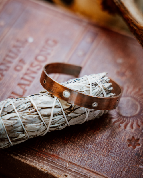 copper cuff with silver rivets sitting on a sage stick on old books