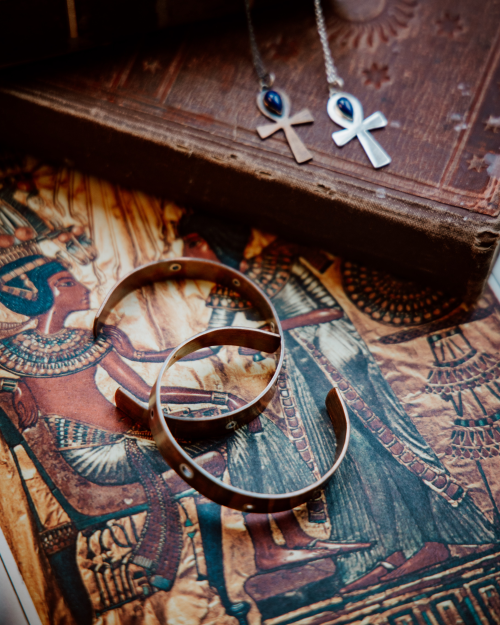 2 copper cuffs with silver rivets sitting on a sage stick on old books