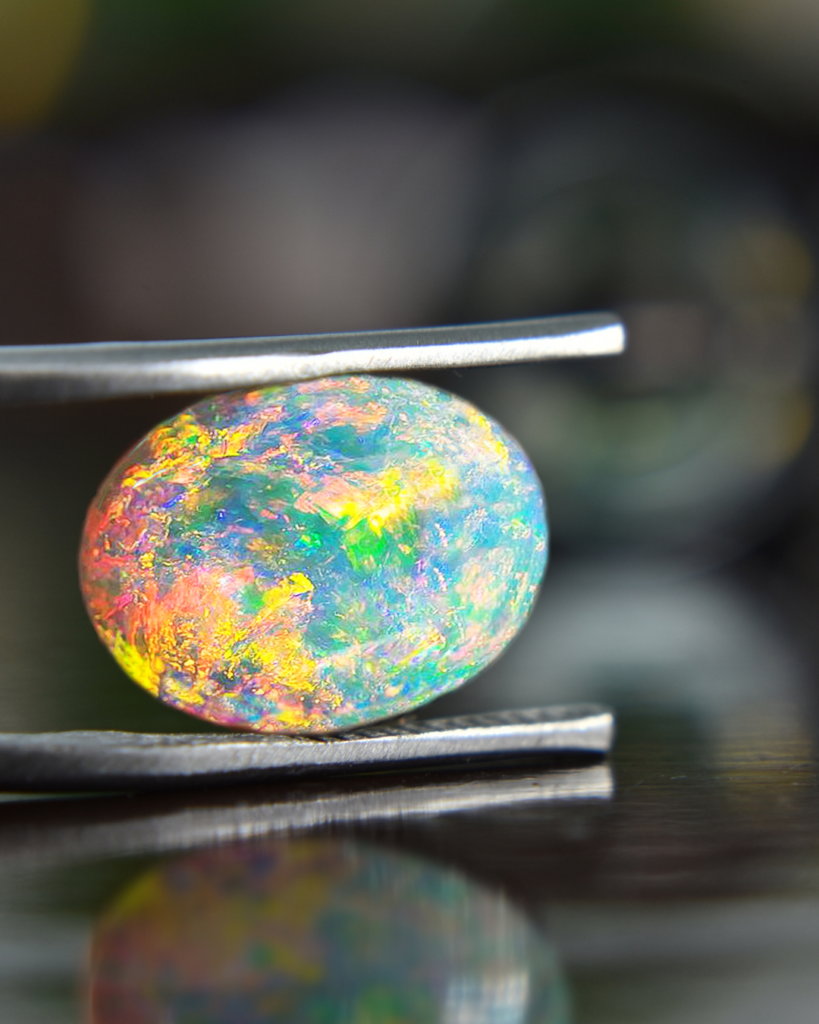 rainbow effect opal gemstone in tweezers