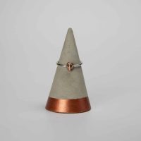 tiny copper skull on a silver band sat on a grey concrete cone with copper base and white background