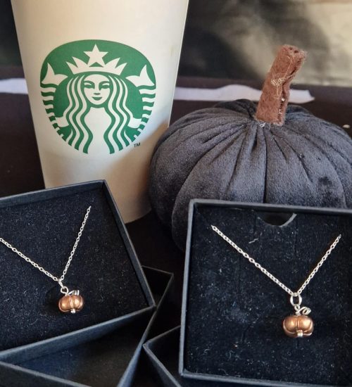 Two copper pumpkin necklaces displayed in front of a black velvet pumpkin and a Starbucks coffee cup
