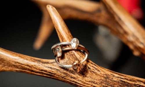 3 small skull rings made from copper and silver hung on antlers with a red candle in the background