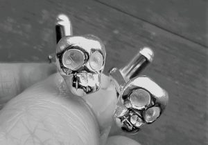 memento mori skull cufflinks held in hand with wood background