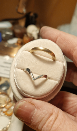 a hand holding a pink ring oval ring box with a brushed gold wedding band and a silver wishbone ring